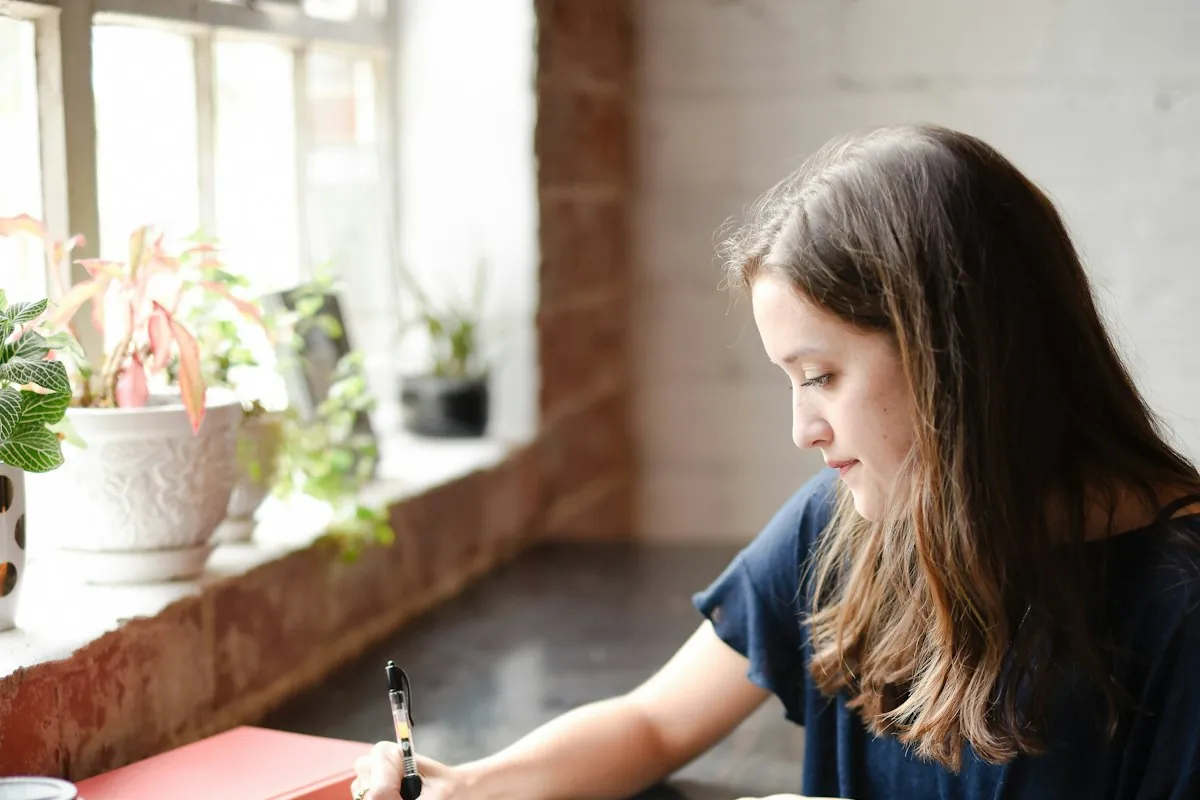 A woman writing at a table by a window